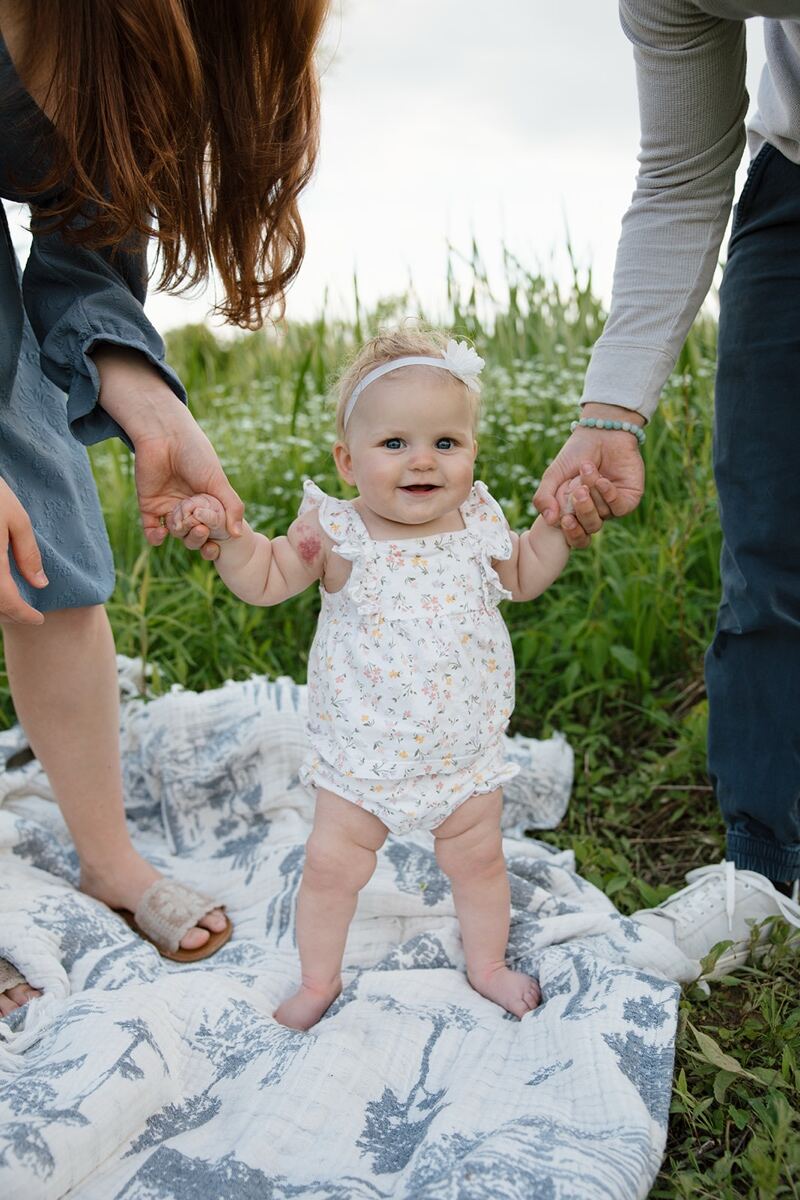 Adeline standing outdoors holding her parents' hands